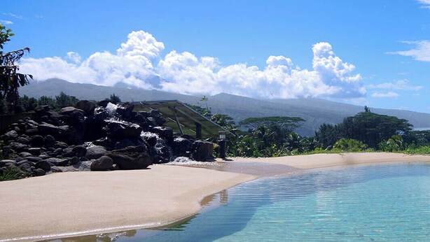 Una piscina cristallina circondata da una spiaggia sabbiosa e una vegetazione rigogliosa, con montagne sullo sfondo.