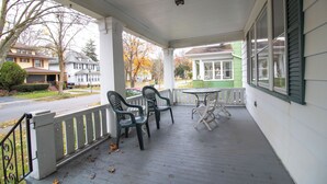 Ein überdachter Balkon mit Tisch und Stühlen, einem Geländer und Blick auf die Straße und die Häuser.