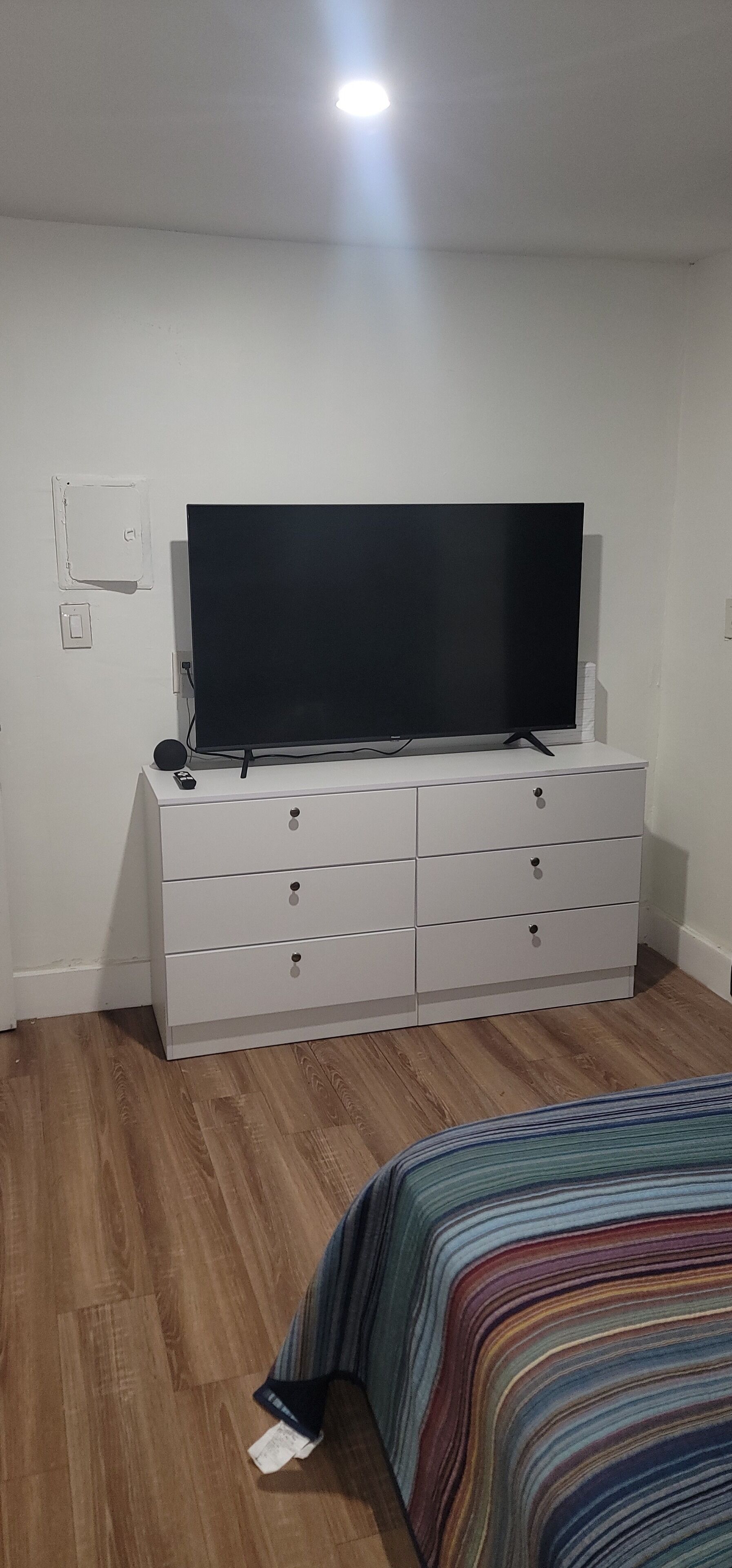 A bedroom with a white dresser, a flat-screen TV, and a striped bedspread.