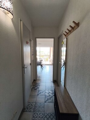 Un pasillo con baldosas estampadas, un banco y una puerta que da a un balcón con mobiliario exterior.