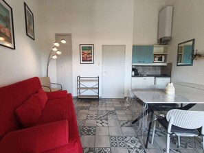 Um espaço de estar compacto com um sofá vermelho, uma mesa de jantar com cadeiras, uma cozinha compacta e ladrilhos de chão estampados.