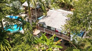 Un resort tropical con piscina, palmeras y una cabaña con techo de paja.