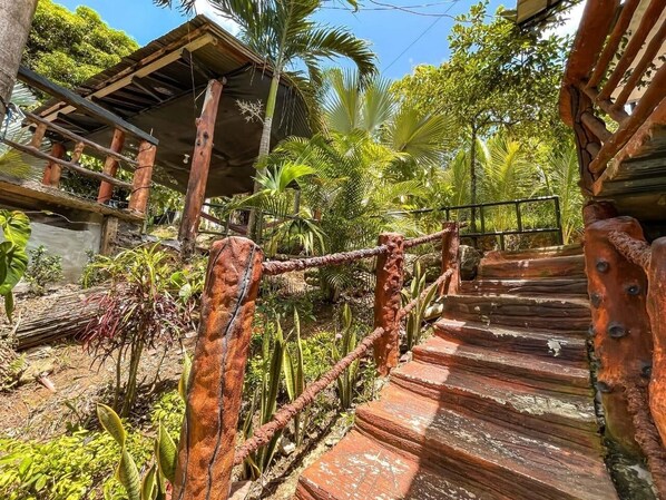 Eine rustikale Holztreppe mit Metallgeländer, umgeben von üppigem Grün und Palmen.