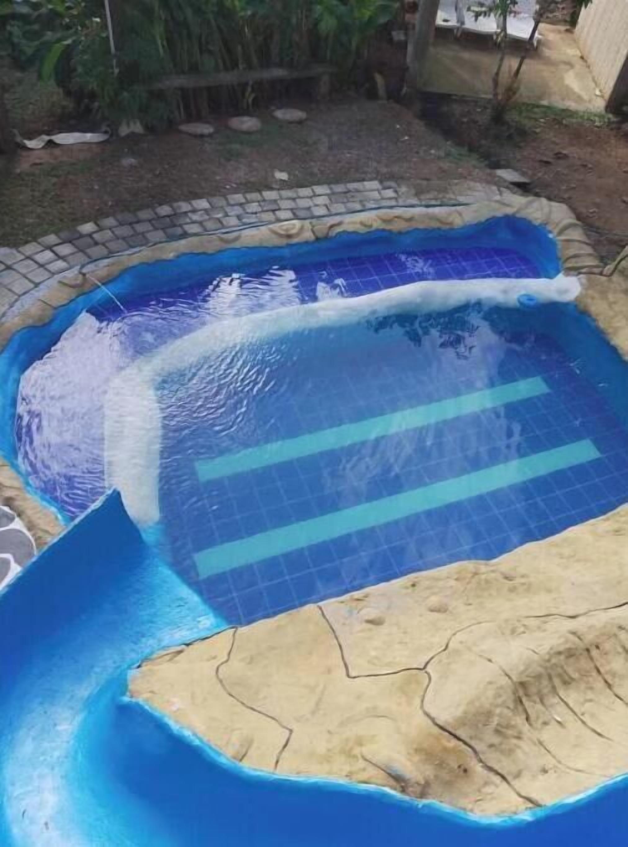 A swimming pool with blue tiles and a sandy area.