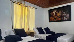 Habitación de hotel con dos camas, ropa blanca, almohadas azul oscuro y un cuadro de caballos en la pared, además de un techo de madera.