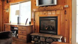 A wooden interior with a fireplace, a television mounted above it, and a desk with drawers and a lamp. - Sugar Bear (Big Bear City)