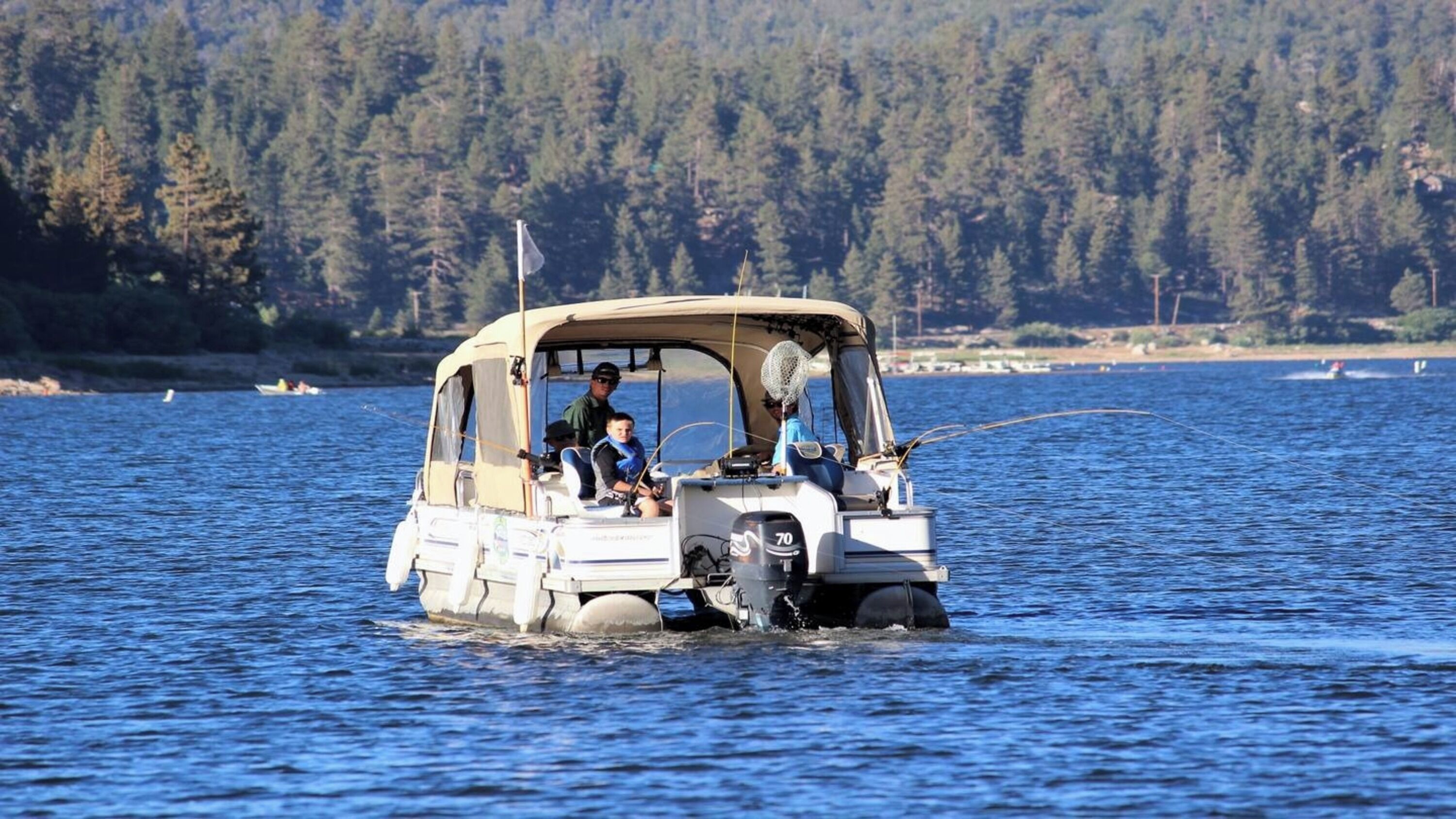 Ein kleines Boot mit Verdeck, zwei Personen an Bord und eine bewaldete Uferlinie im Hintergrund.