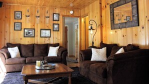 A cozy living room with wooden walls, two brown sofas, a coffee table, and framed pictures. - Sugar Bear (Big Bear City)