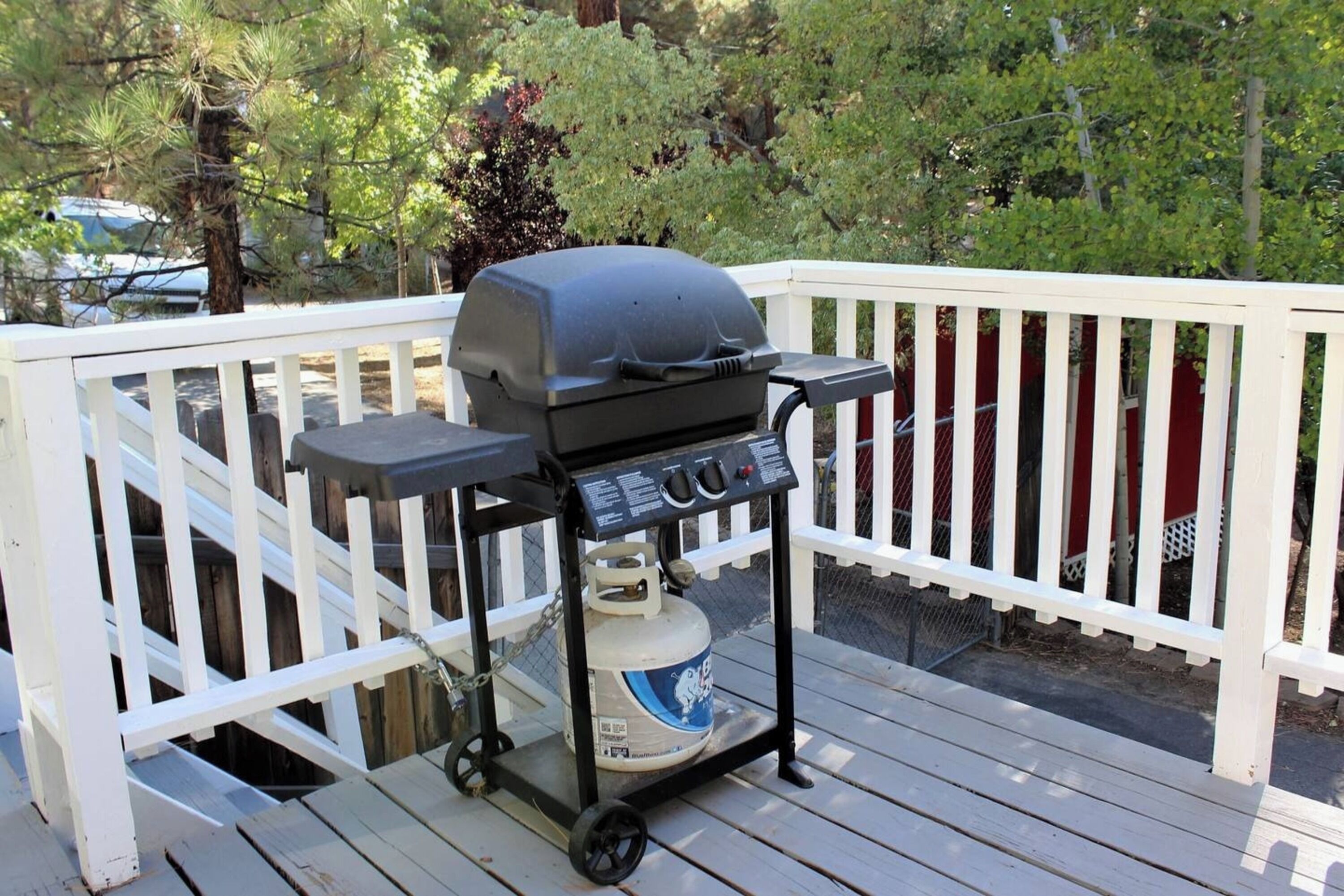 A barbecue grill on a wooden deck with a white railing.