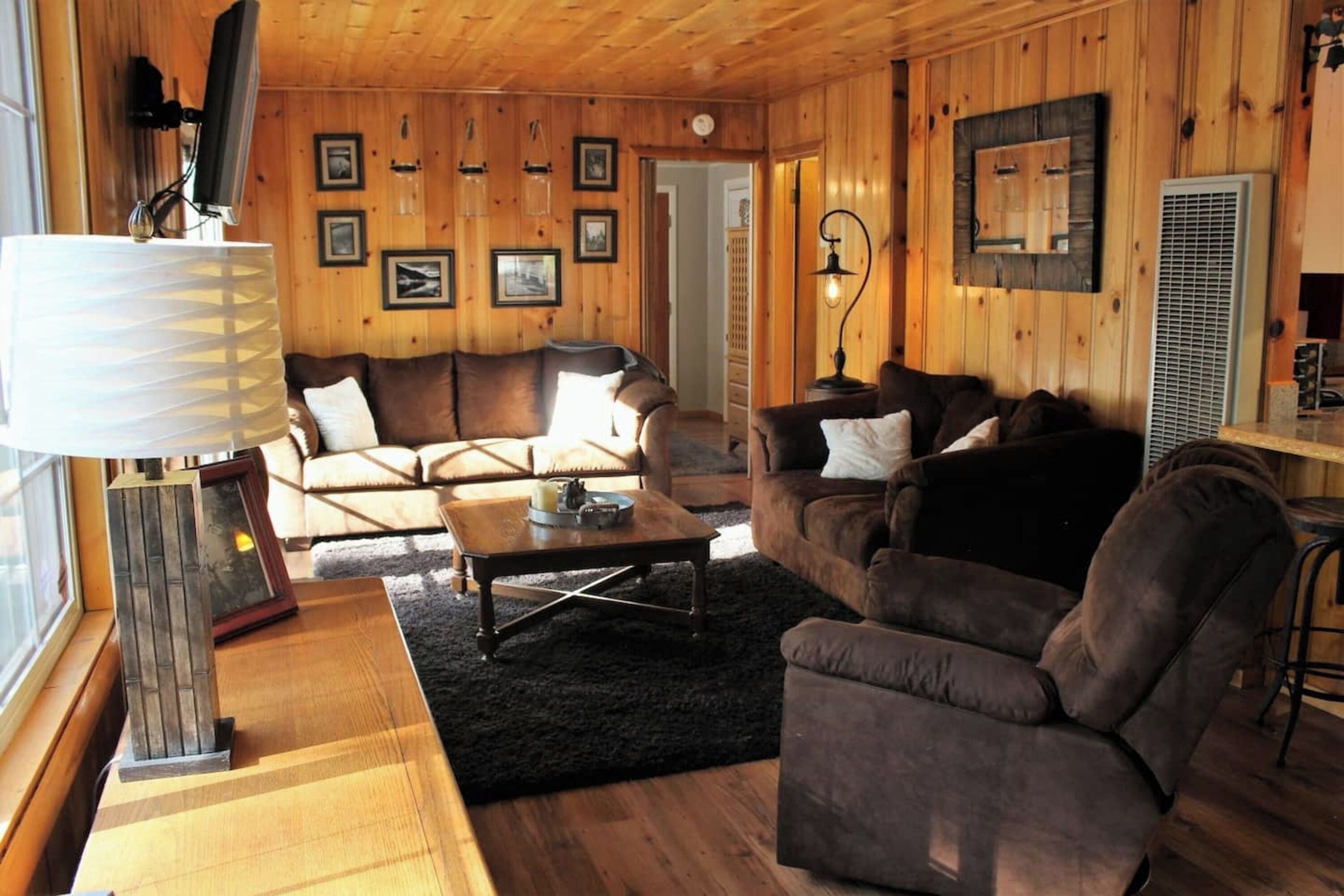 Una sala de estar acogedora con paredes de madera, un sofá marrón, una mesita de centro y un televisor.