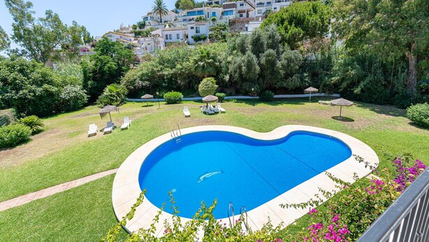 A heart-shaped swimming pool with a clear blue water, surrounded by a well-maintained lawn and a variety of plants. - Townhouse Cortijos de La Hidalga (Benalmádena)