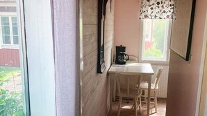 A narrow room with a table, chairs, a coffee maker, and a window with a floral curtain. - 4 Person Holiday Home in Steninge (Steninge)