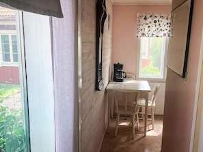 A narrow room with a table, chairs, a coffee maker, and a window with a floral curtain.