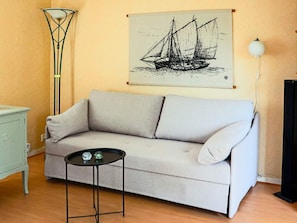 A living room with a sofa, a small table, a floor lamp, and a wall-mounted artwork of a sailing ship. - 4 Person Holiday Home in Steninge (Steninge)