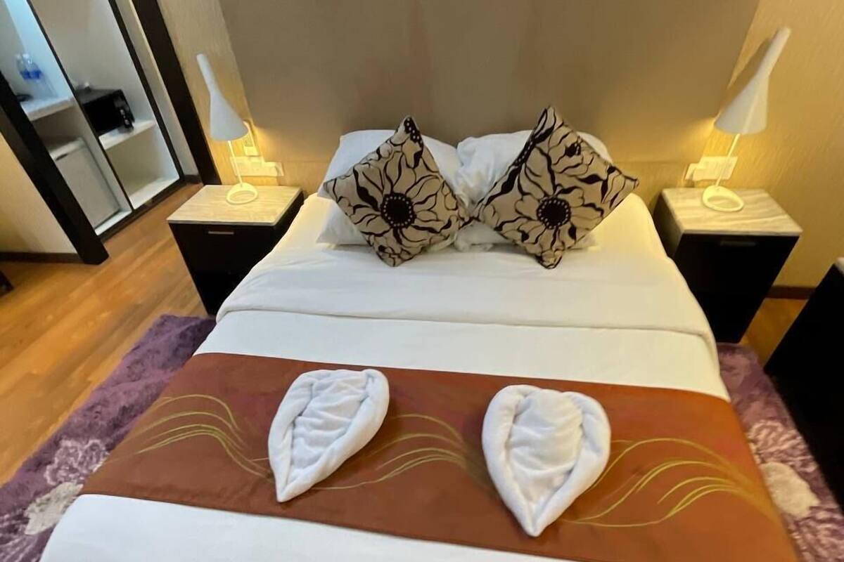 Un lit bien fait, avec une tête de lit marron, du linge de lit blanc et deux coussins décoratifs.