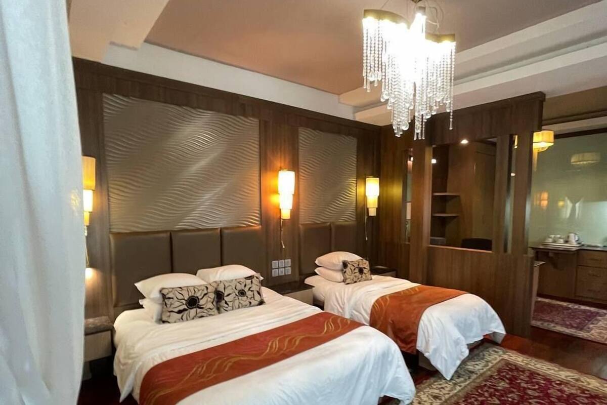Une chambre d’hôtel avec deux lits, un lustre et un tapis rouge à motifs.