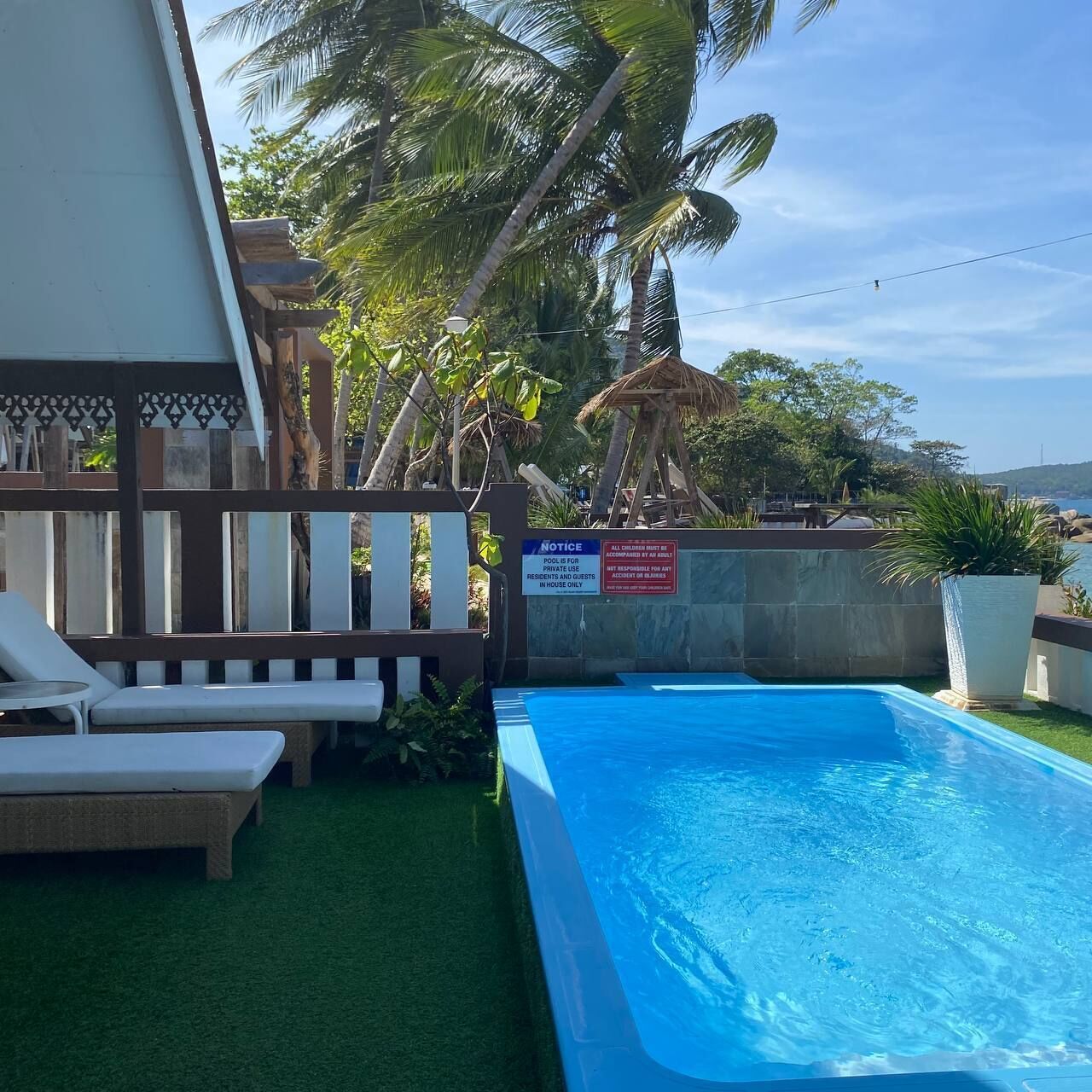 Zona de piscina con valla de madera, sillas de descanso y un letrero que indica que el uso de la piscina es exclusivo para residentes e invitados.