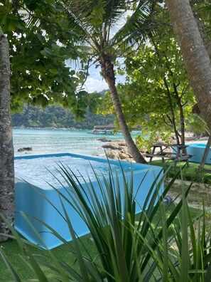 A swimming pool surrounded by lush greenery and a clear view of the sea. - Coralview Bluestar Perhentian  (Pulau Perhentian Besar)