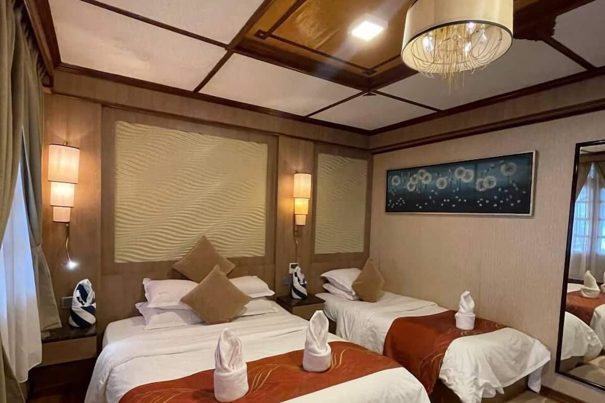 Une chambre d’hôtel avec deux lits, un lustre, un grand miroir et une moquette à motifs floraux.