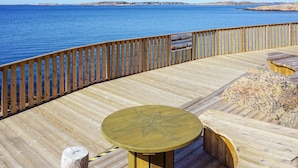 Een houten terras met een ster-vormige tafel en banken, uitkijkend op een wateroppervlak.