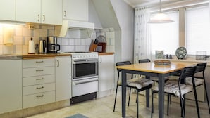 Een moderne keuken met witte kasten, een inbouwoven en een eethoek met een houten tafel en zwarte stoelen.