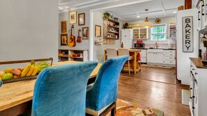 A dining area with a wooden table, blue chairs, and a fruit bowl. There is a kitchen in the background with white cabinets and a sign that says "BAKERY". - Family & Friends - Fun In Franklin (Franklin)