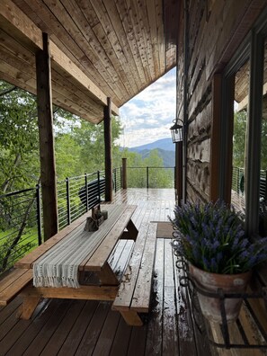 A wooden deck with a bench and potted plants, overlooking a mountainous landscape.