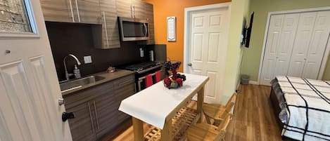 Cozinha compacta com eletrodomésticos modernos, mesa de jantar com cadeiras e um quarto com cama.