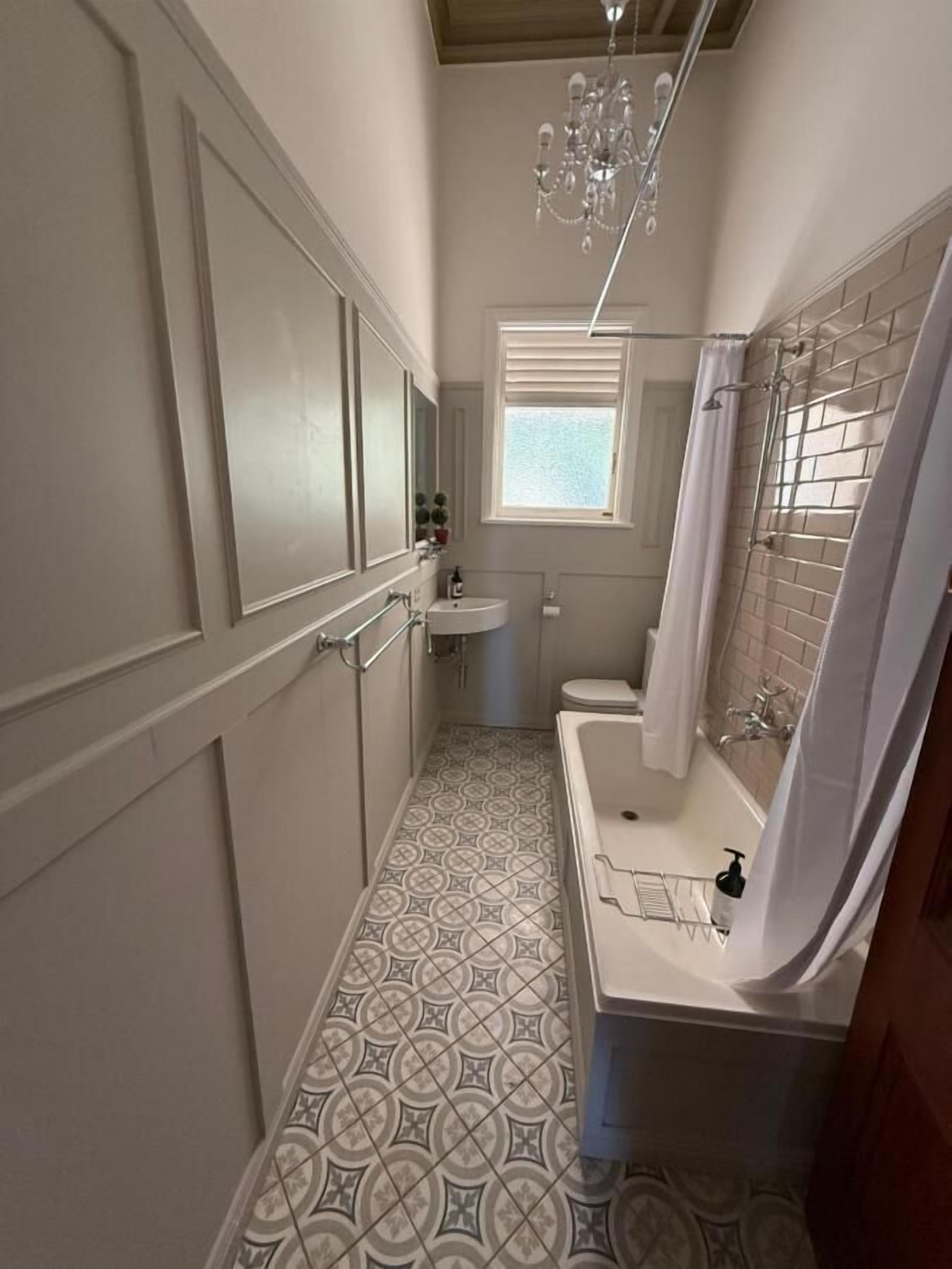 A narrow bathroom with a patterned floor, a sink, a toilet, and a shower area.