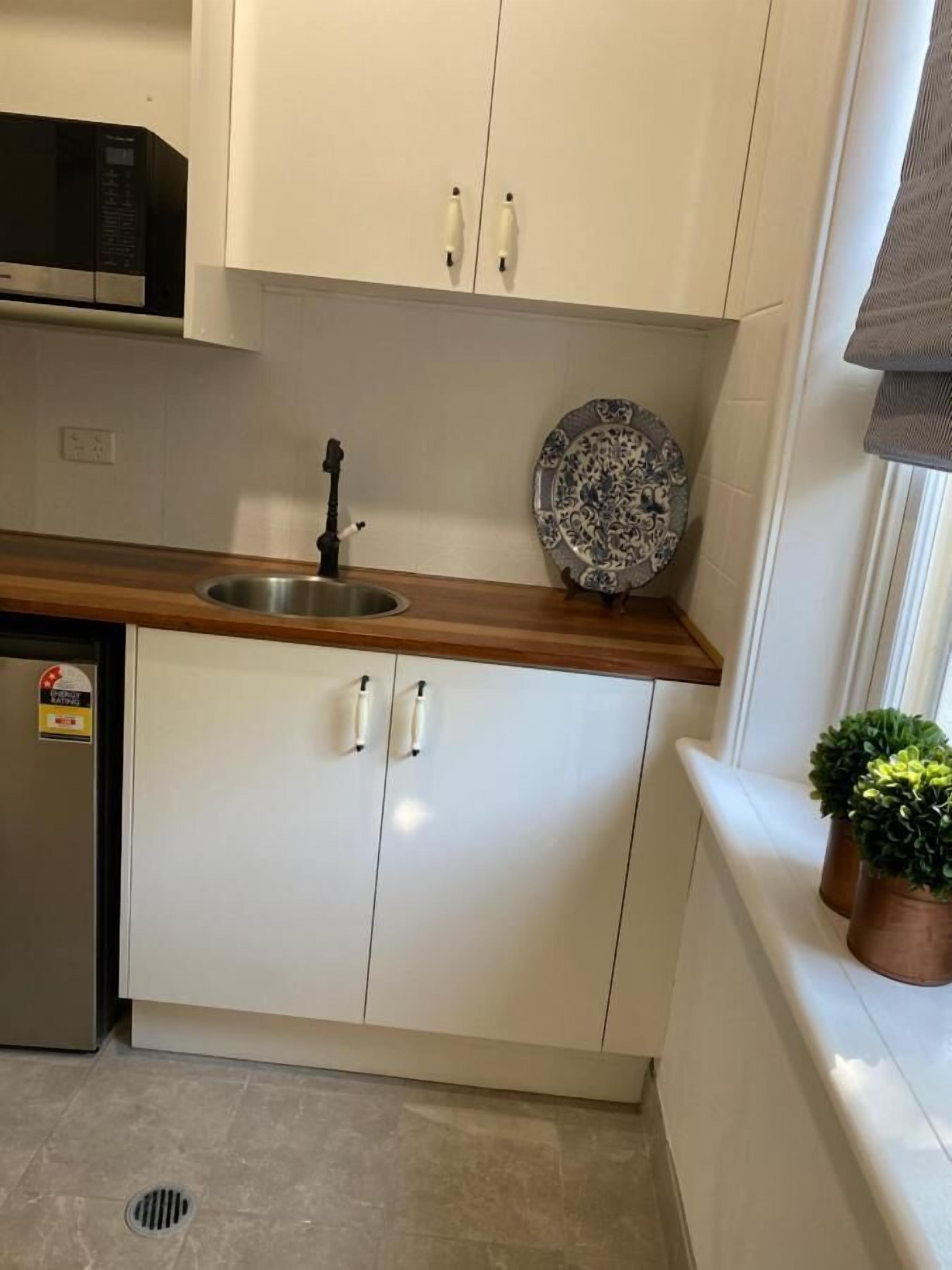 A compact kitchen with white cabinets, a stainless steel sink, a microwave, and a decorative plate.