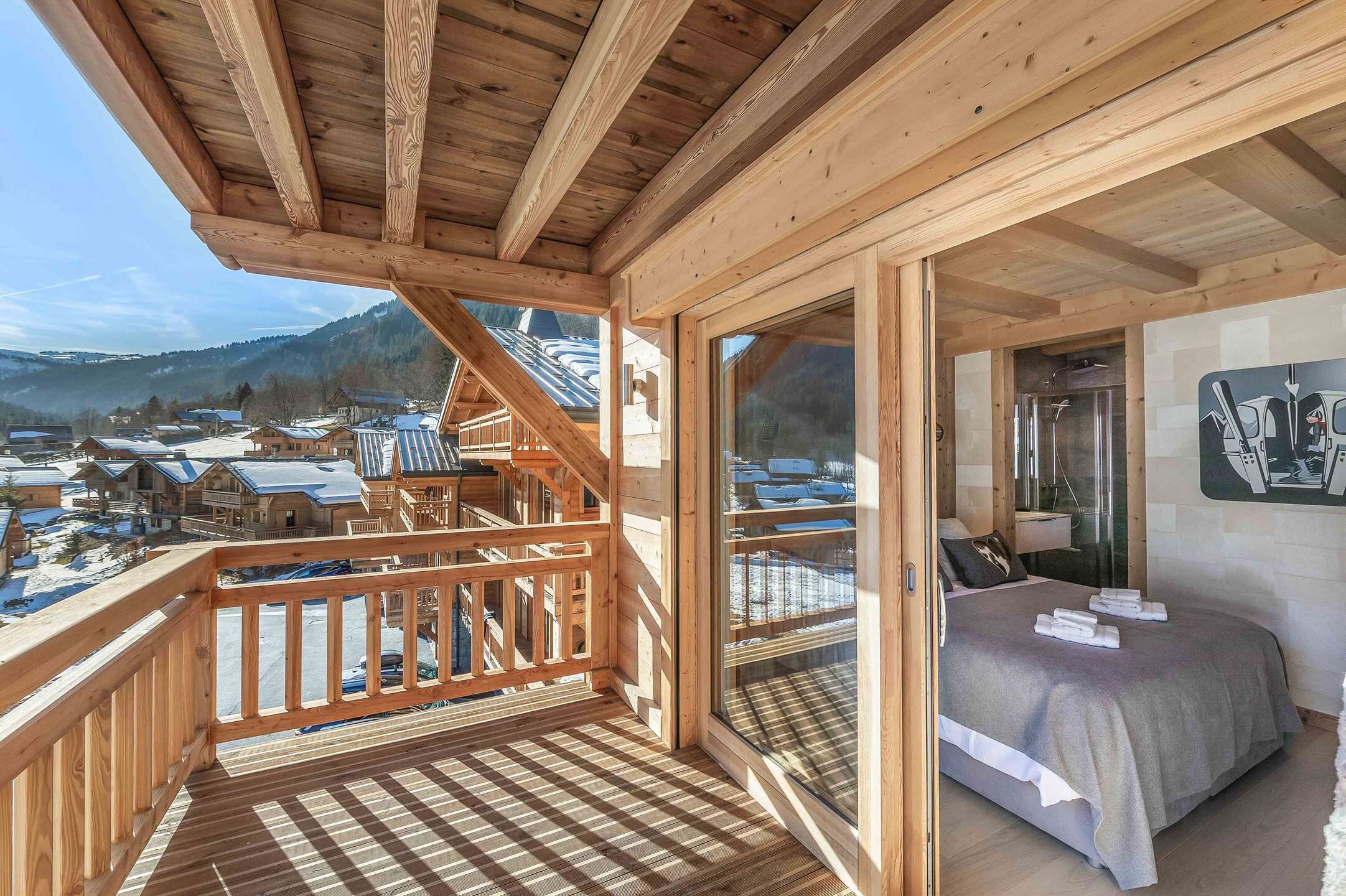Un balcon en bois offrant une vue sur un village enneigé, un lit avec vue et un plafond en bois.