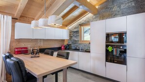 A modern kitchen with white cabinets, a wooden dining table, and a stone wall. - 1/2 Chalet: Alpine sweetness at Linga (CHATEL)