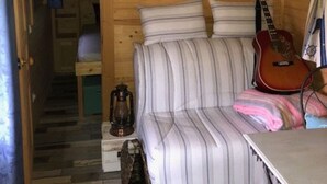 A cozy cabin interior with a wooden ceiling, a striped sofa, a guitar, and a table. - QUIET ROULOTTE on land with swimming pool (Bernay-Saint-Martin)