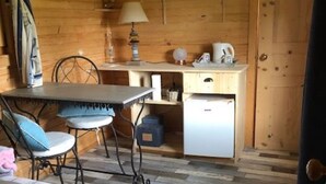 A cozy cabin interior with a wooden floor, a dining table with chairs, a small kitchenette, and a bed with a striped blanket. - QUIET ROULOTTE on land with swimming pool (Bernay-Saint-Martin)
