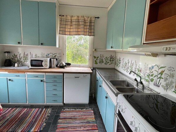 Una cocina compacta con armarios verde mar, un microondas, un hervidor y un lavabo.