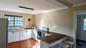 A kitchen with white cabinets, a wooden countertop, a stove, and a window. - Cupie’s Cabin (Talbingo)