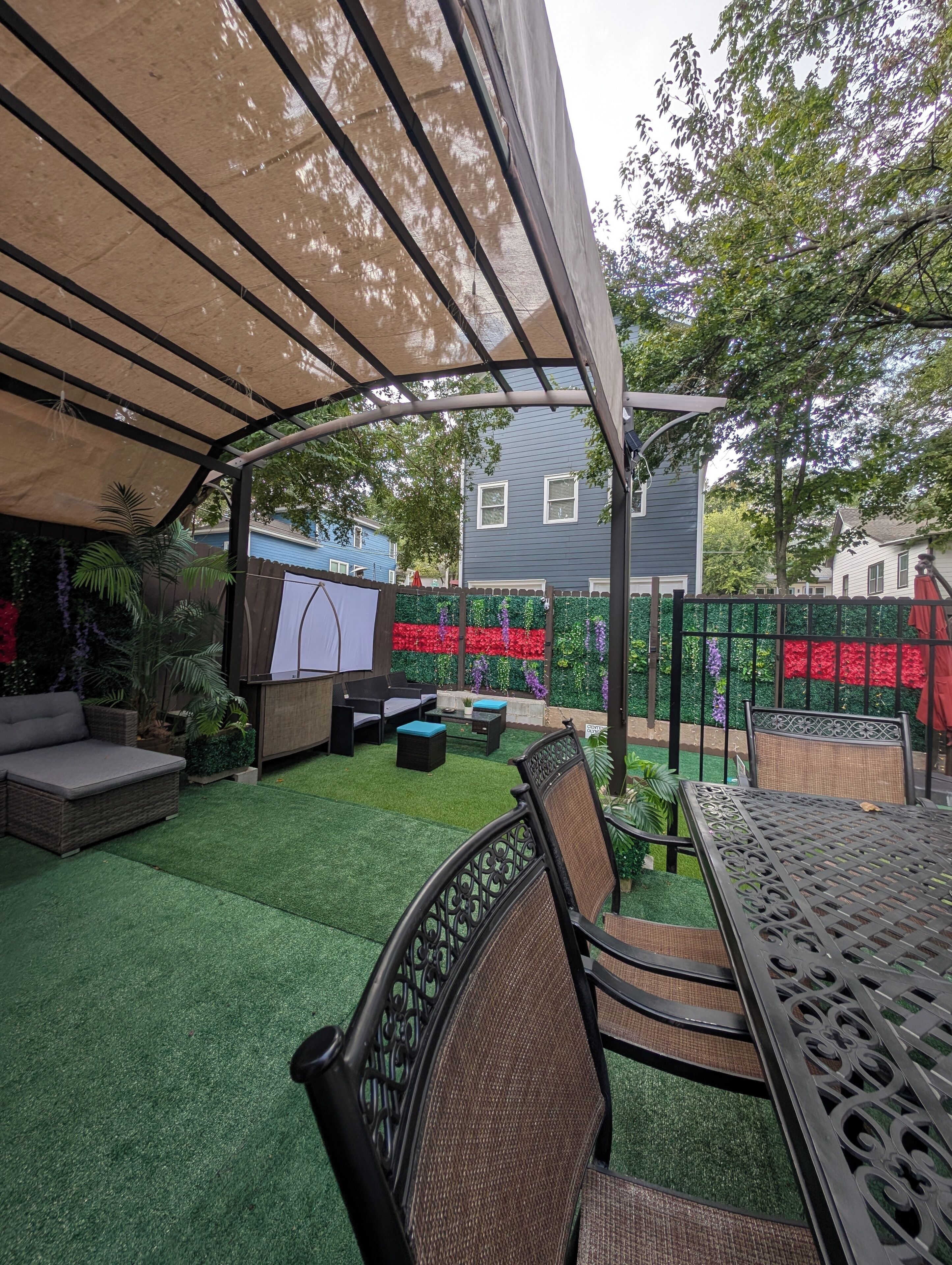 Een overdekt terras met kunstgras, tuinmeubilair en een decoratieve schutting.