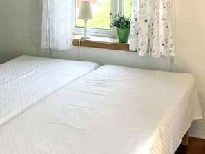 A room with two beds, a window with curtains, a lamp, and a plant on a windowsill. - 2 Person Holiday Home in Odeshog (Odeshog)