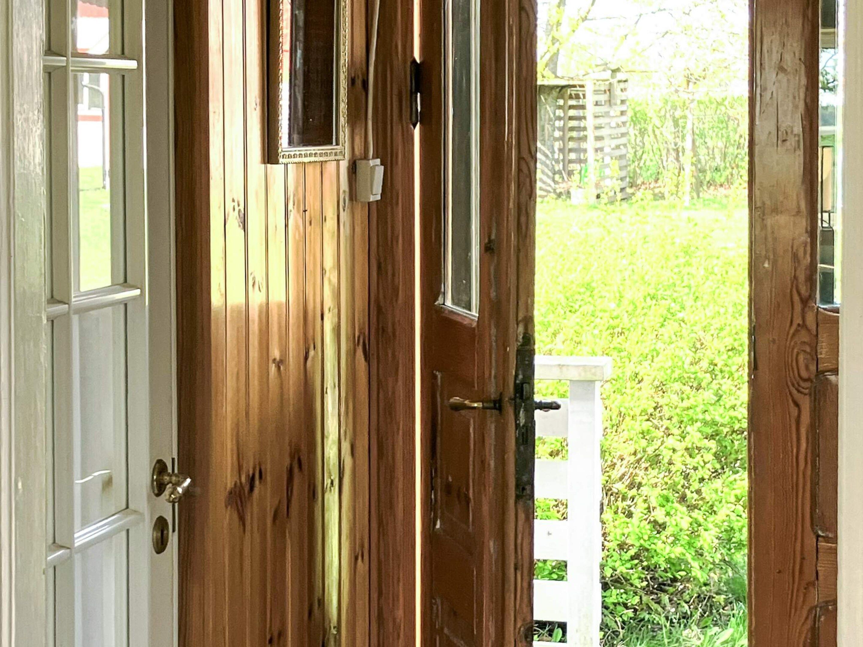 A wooden door with a white frame and a small window, leading to a grassy yard with a white fence.