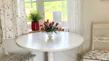 A round white table with a floral vase, two chairs with floral upholstery, and a view of greenery outside.