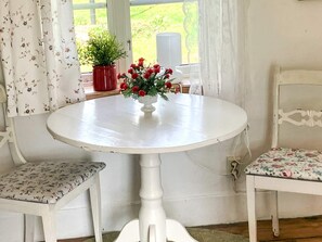 Ett runt, vitt bord med en blomvas, två stolar med blommigt tyg och utsikt över grönskan utanför.