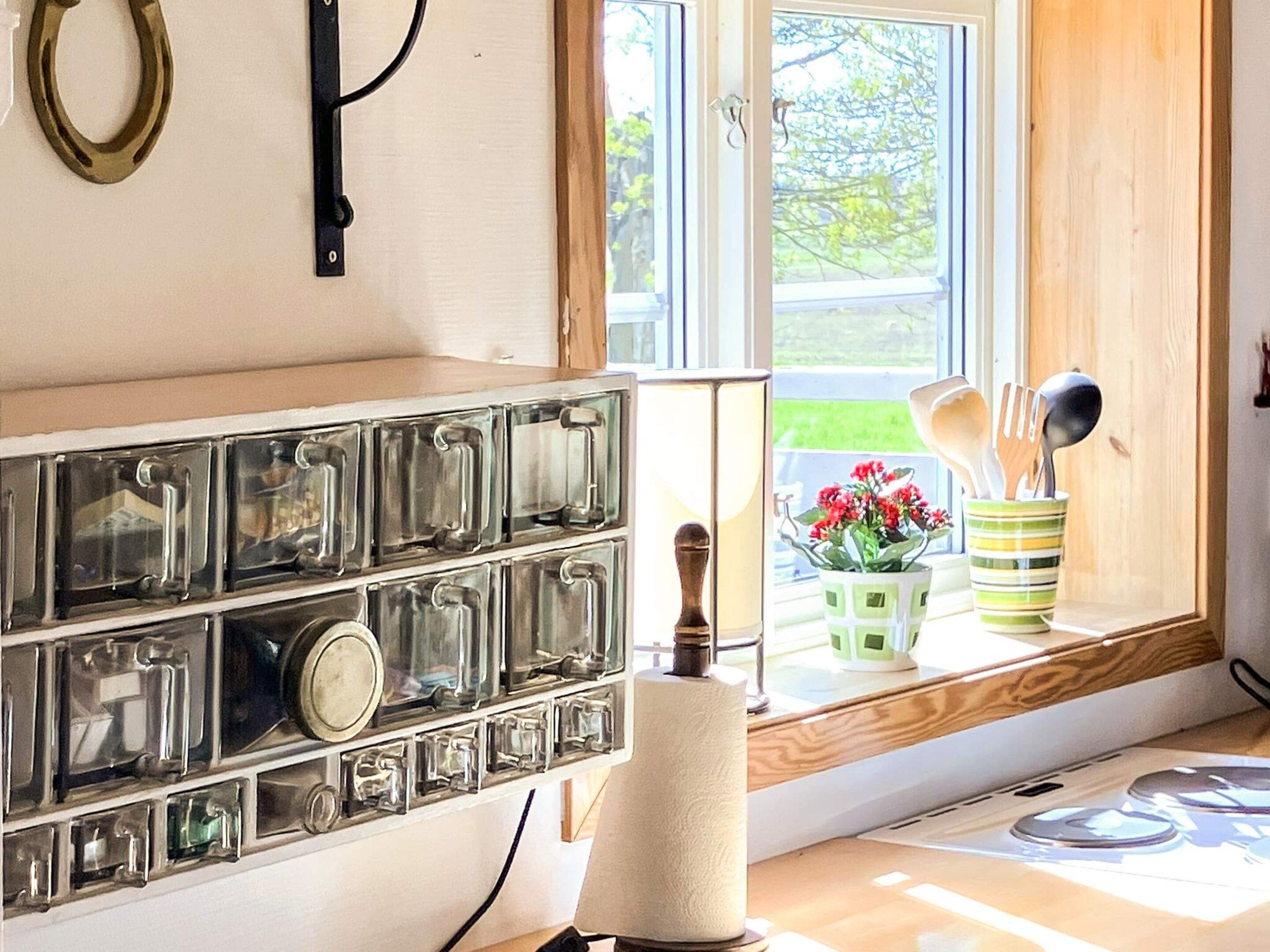 A kitchen with a built-in spice rack, a window with a view of greenery, and a window sill with utensils and a plant.
