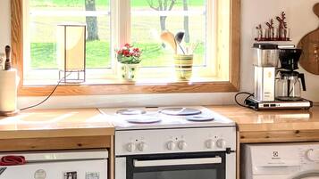 A kitchen with a stove, oven, and washing machine, a window with a view of greenery, and a coffee maker on the counter.