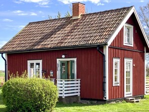 Ett rött trähus med ett sluttande tak, vita fönsterramar och en liten veranda med ett vitt räcke.