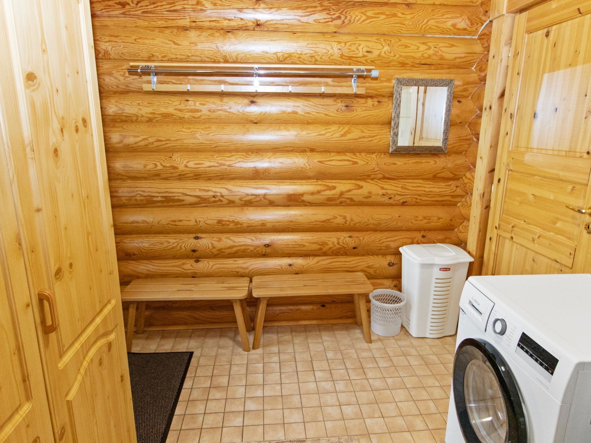 Interior de una cabaña de madera con un banco, lavadora y un pequeño armario.