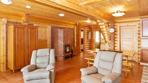 Ein rustikales Holzhaus-Interieur mit zwei Sesseln, einem Kamin, Holzwänden und einer Treppe.