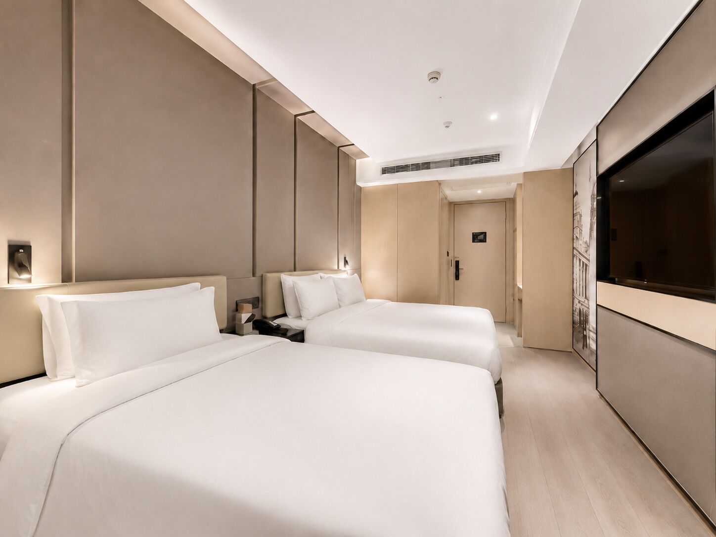 Habitación de hotel con dos camas, un televisor, una puerta y una lámpara fijada a la pared.