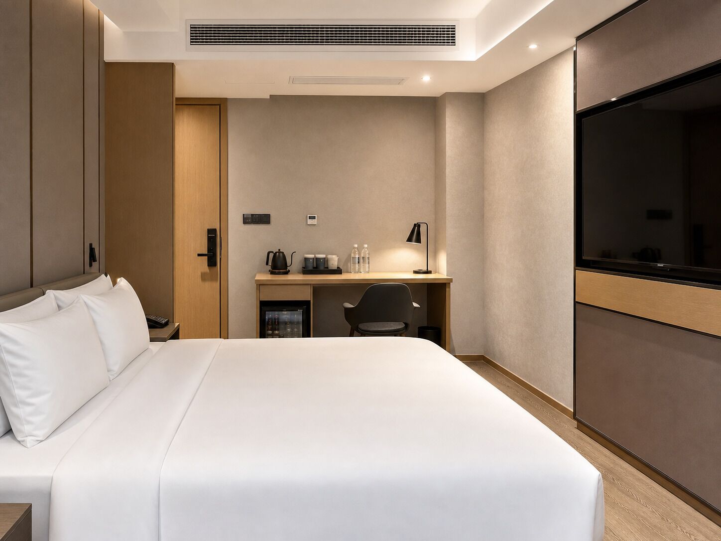 A hotel room with a bed, a desk, a chair, a television, and a minibar.