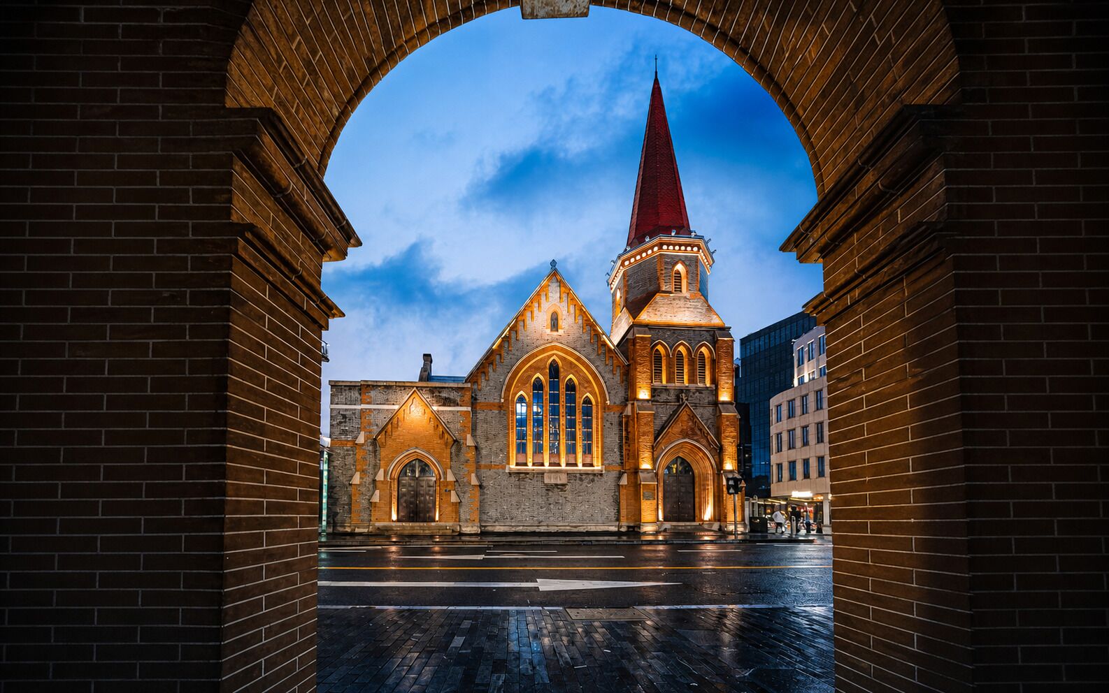 Une église dotée d’un clocher imposant et d’une entrée en arc de cercle, entourée d’immeubles en briques.