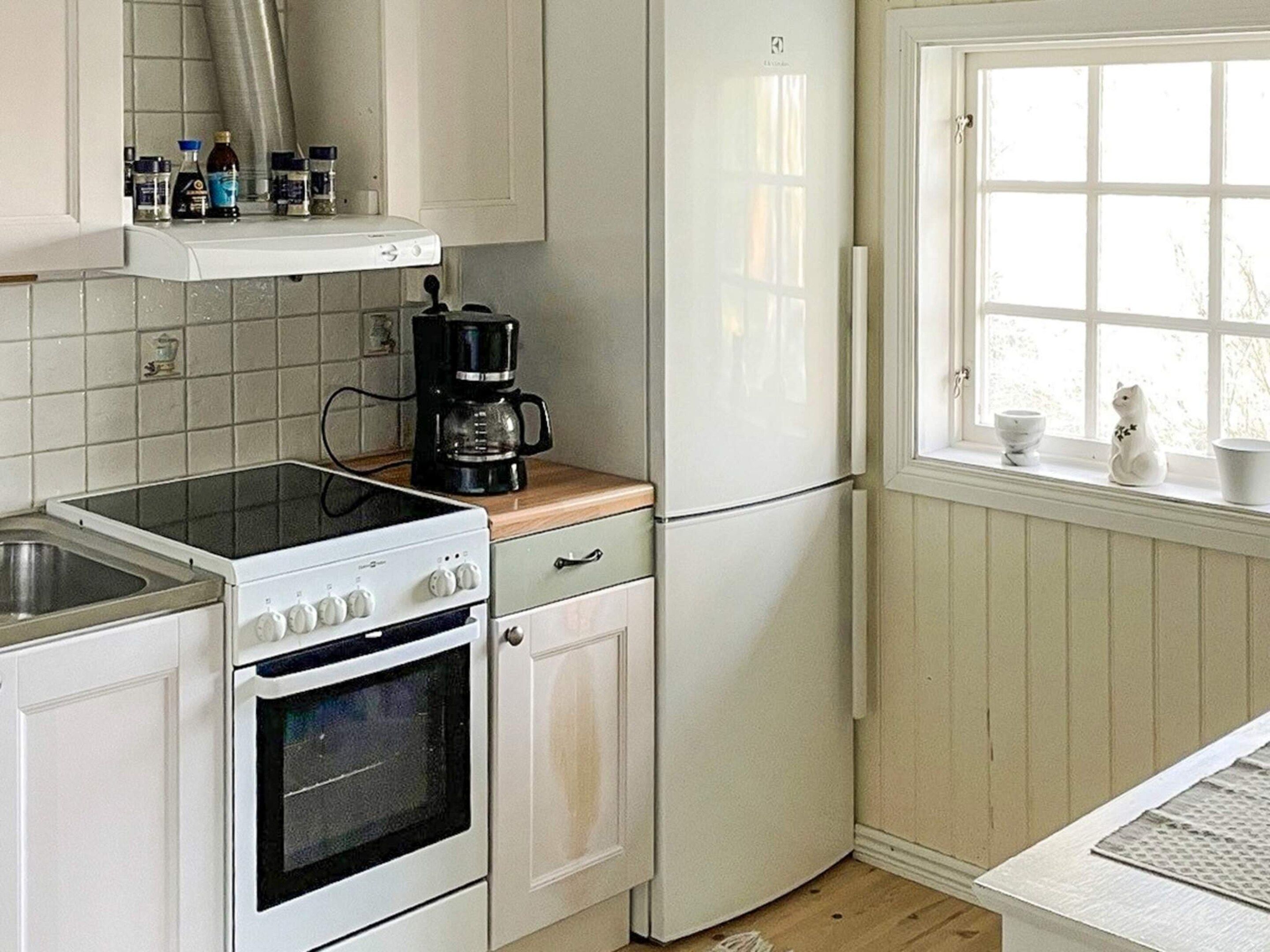 A kitchen with white cabinets, a stove, a coffee maker, and a window with a view.